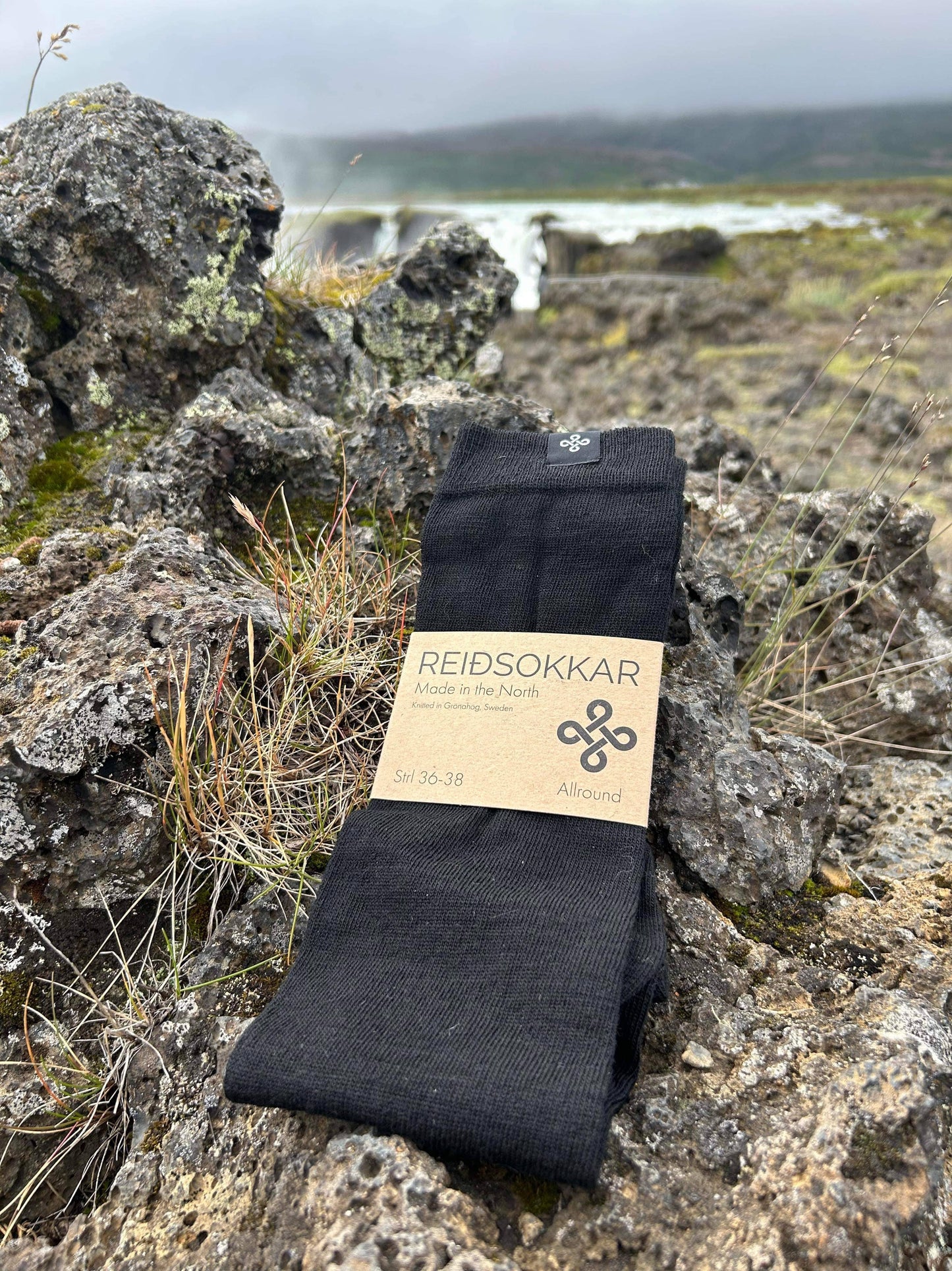 Reidsokkar Sleipner Svart i merinoull som ligger på en stenhäll på island